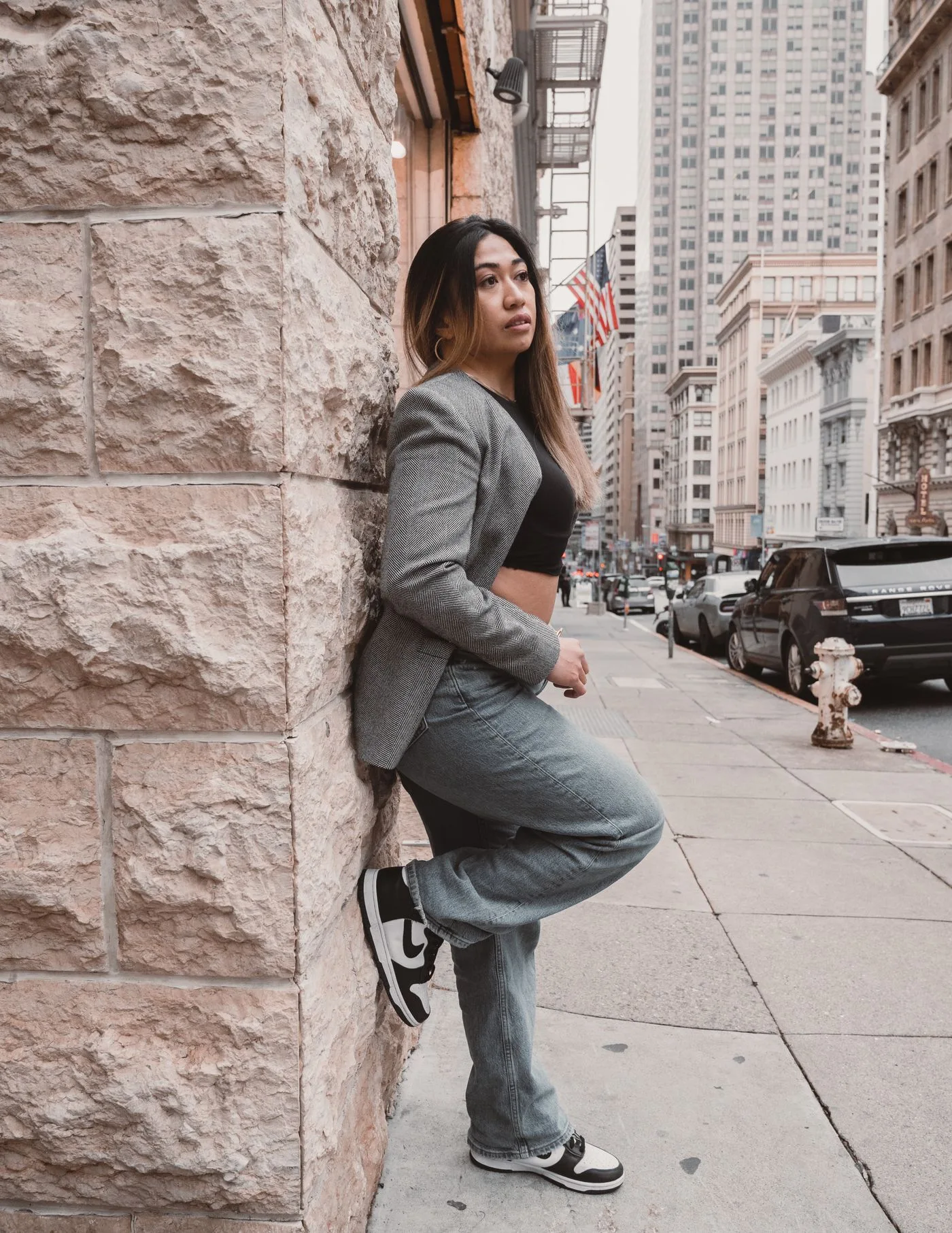 A woman wearing a blazer poses on a city street.