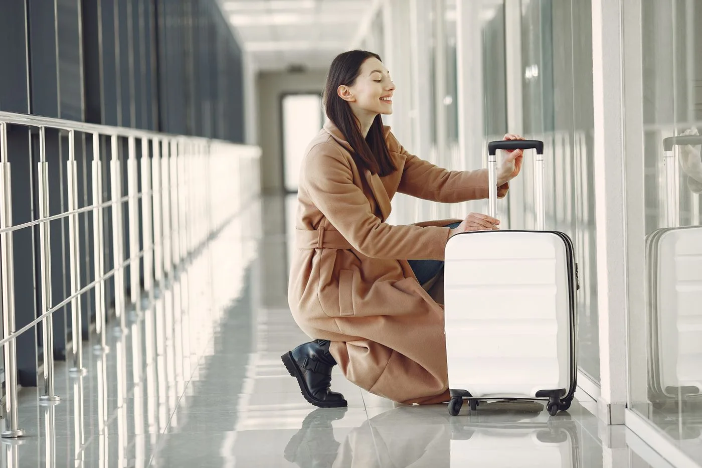 A woman with a suitcase sitting in an airport corridor.