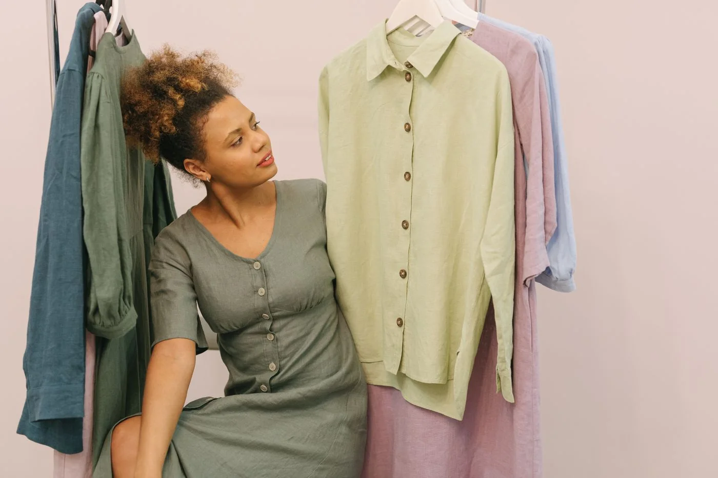 Woman browsing light-colored garments hanging in a clothing boutique.