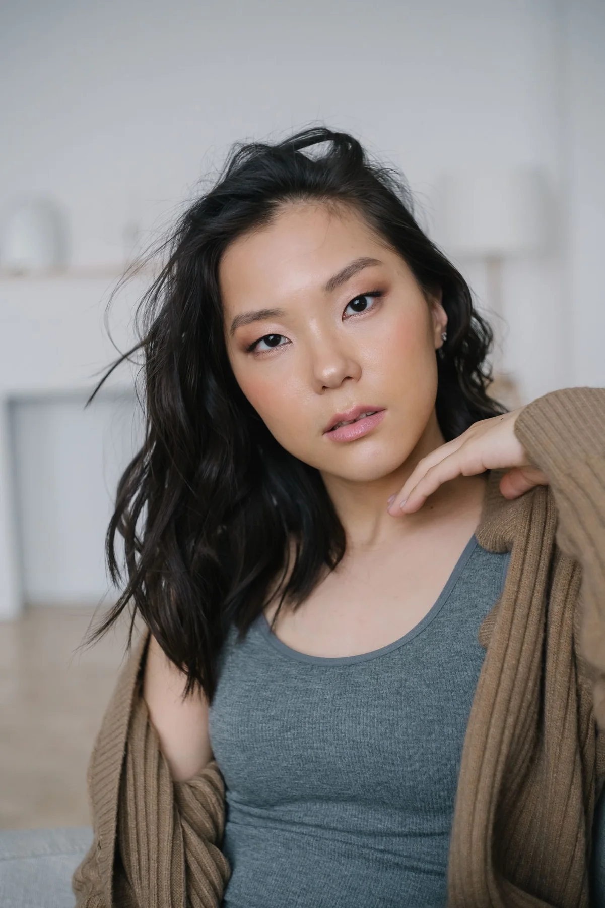 A woman wearing an open brown cardigan over a grey tank indoors.