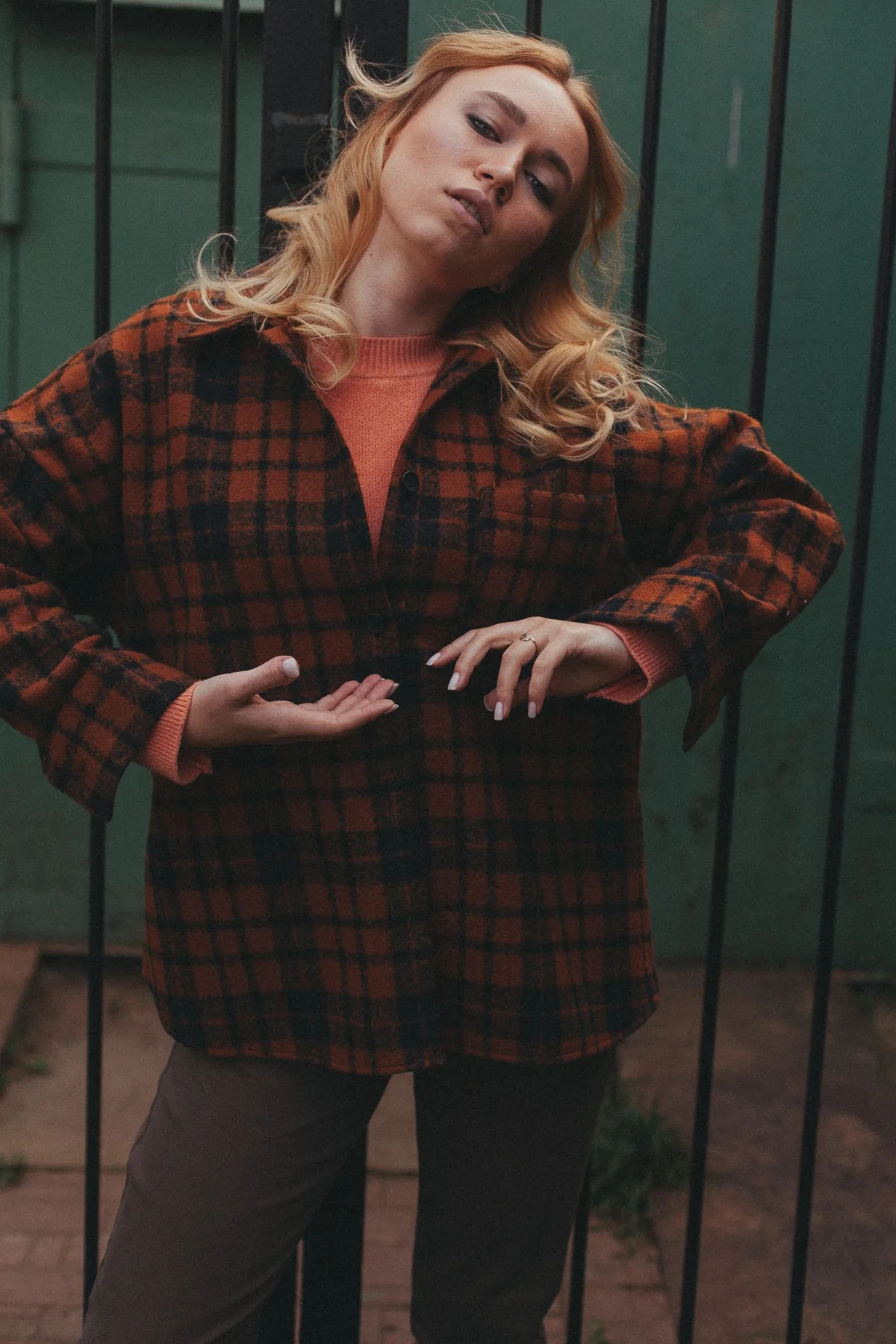 A woman in a belted checked outer layer beside a dark green doorway.