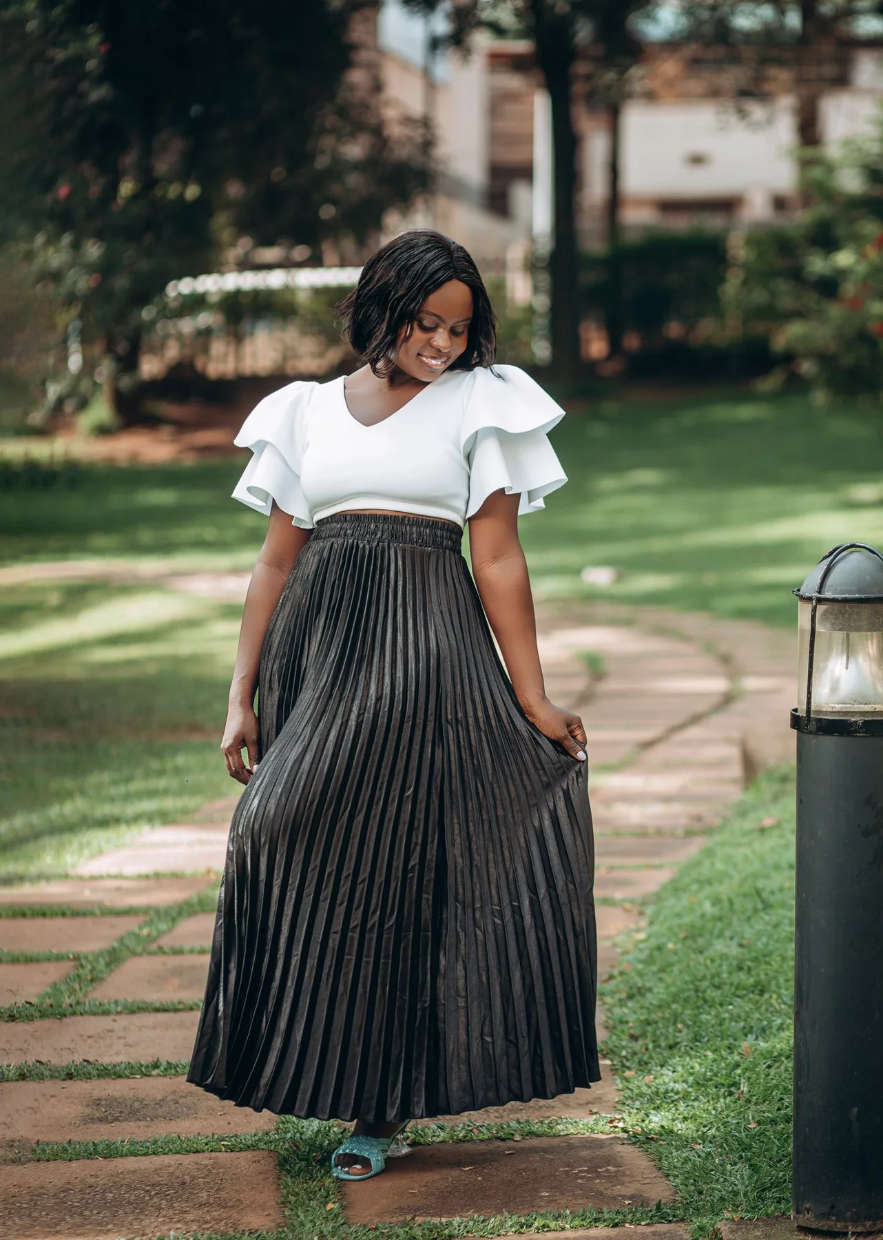 A woman in a long dark pleated skirt and pale top on a park path.