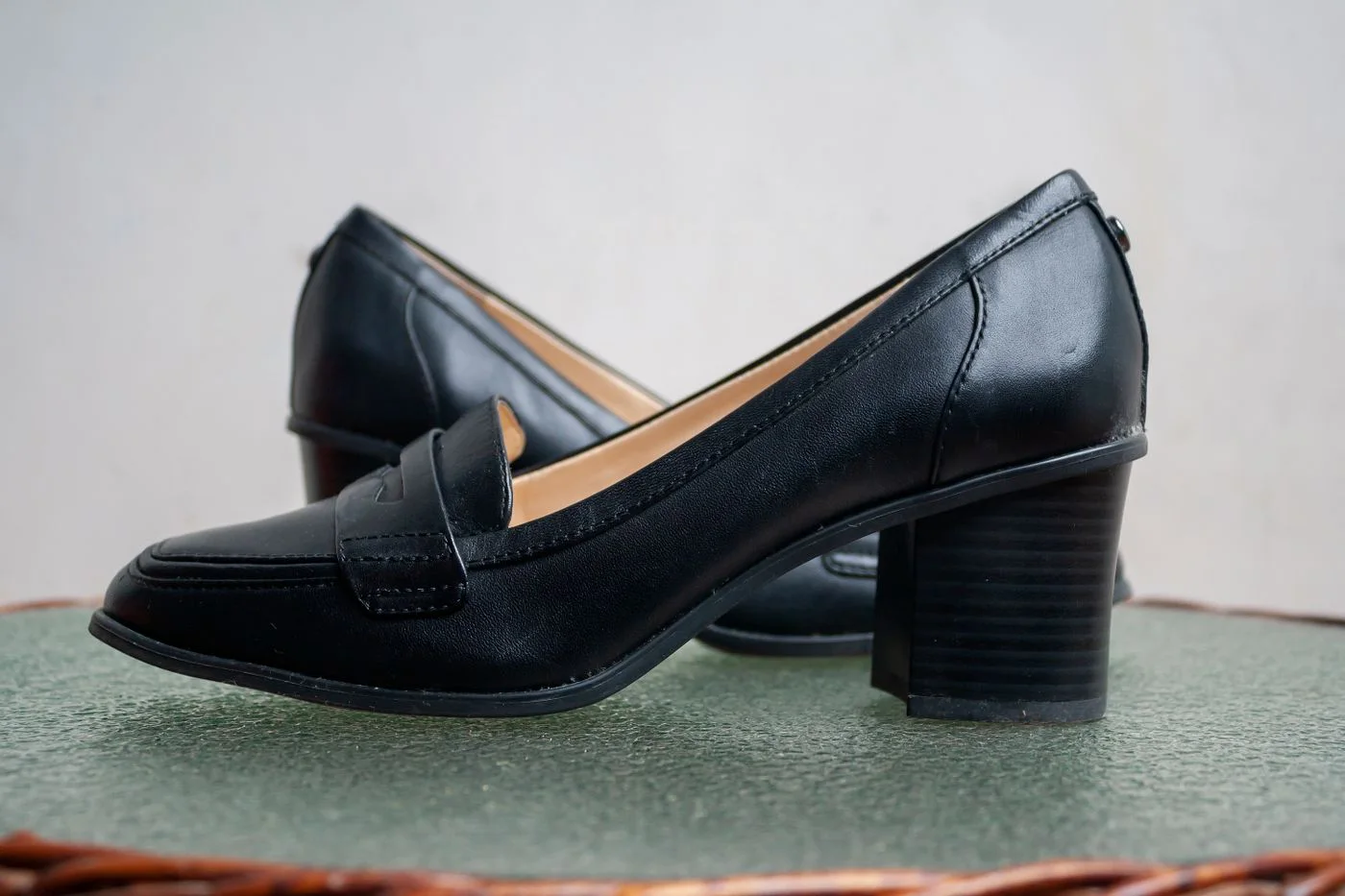 Dark slip-on shoes with low block heels on a muted green surface.