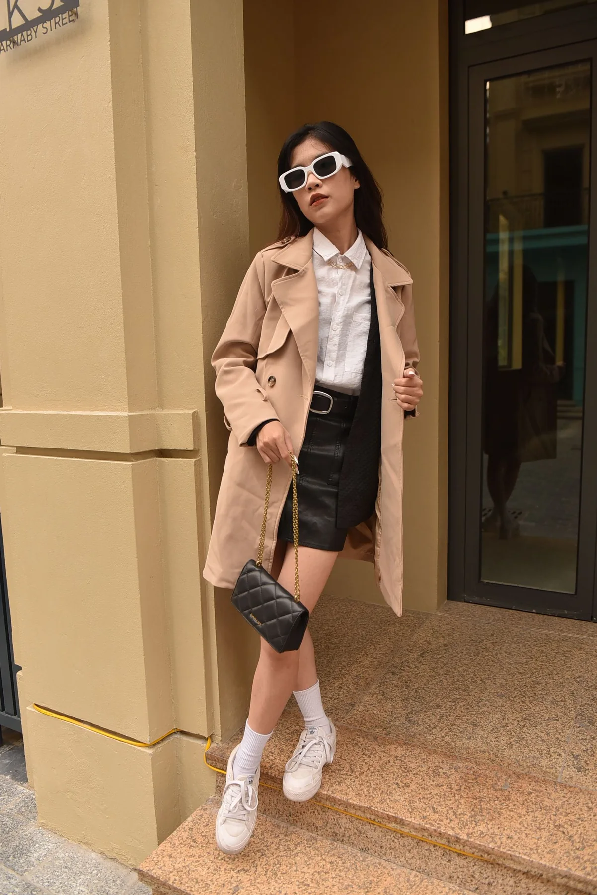 A woman in a pale coat and dark skirt beside a doorway.