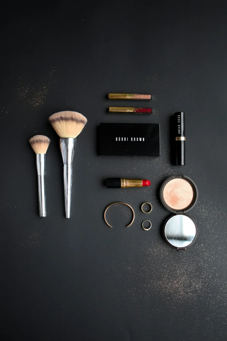 Makeup brushes and cosmetic products arranged against a dark background.