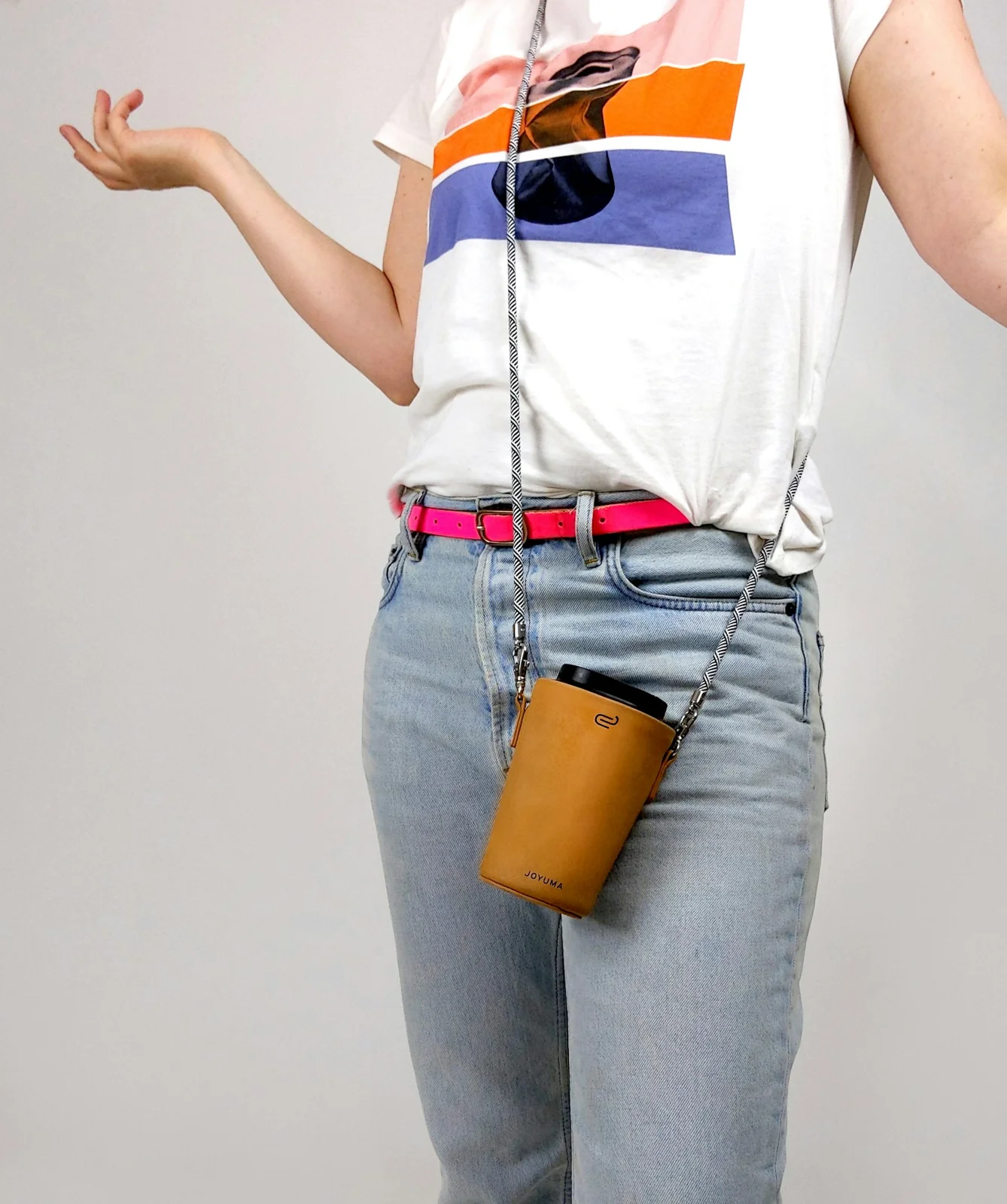 A mustard-coloured cup carrier on a crossbody cord over a printed T-shirt and jeans.