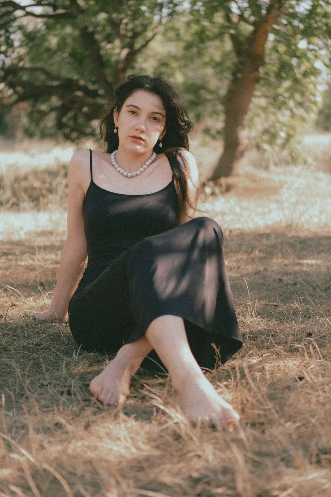 Woman in a black slip dress seated on grass outdoors