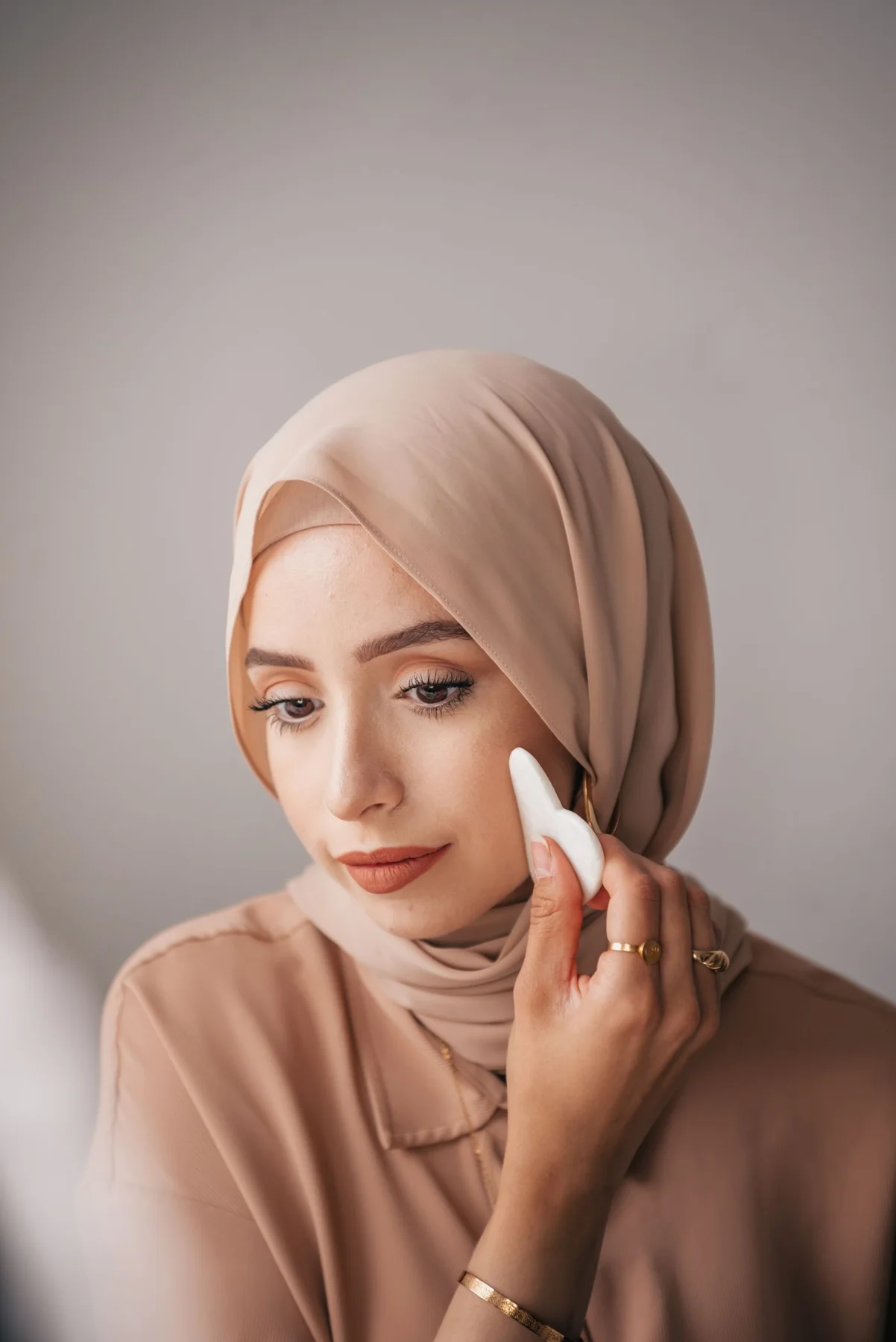 A woman in a headscarf applying makeup with a sponge.