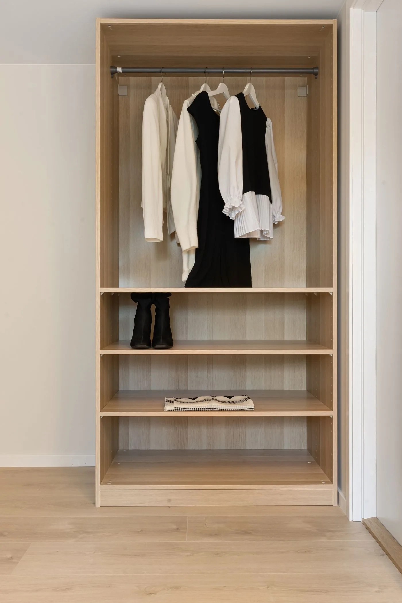 An open wooden wardrobe with hanging clothes and shelves.