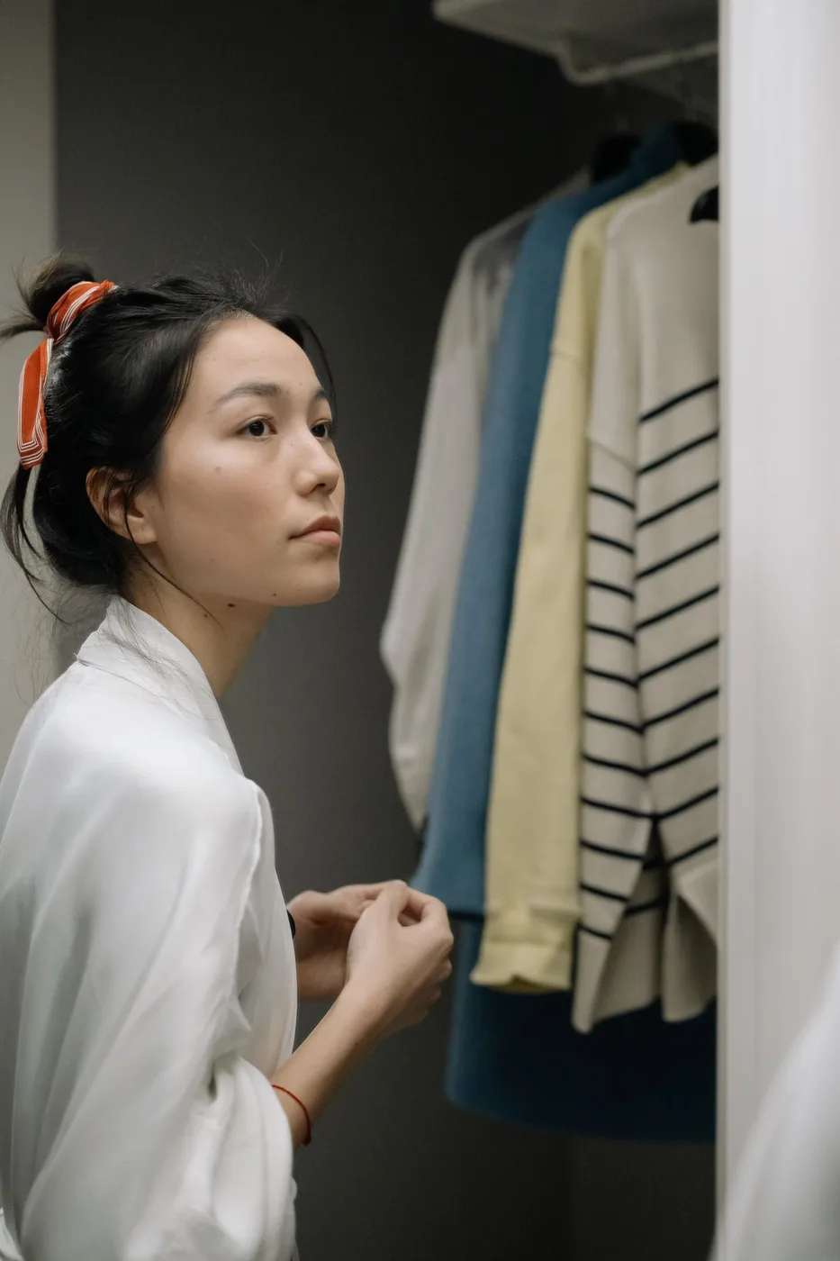Woman considering clothing beside an open wardrobe