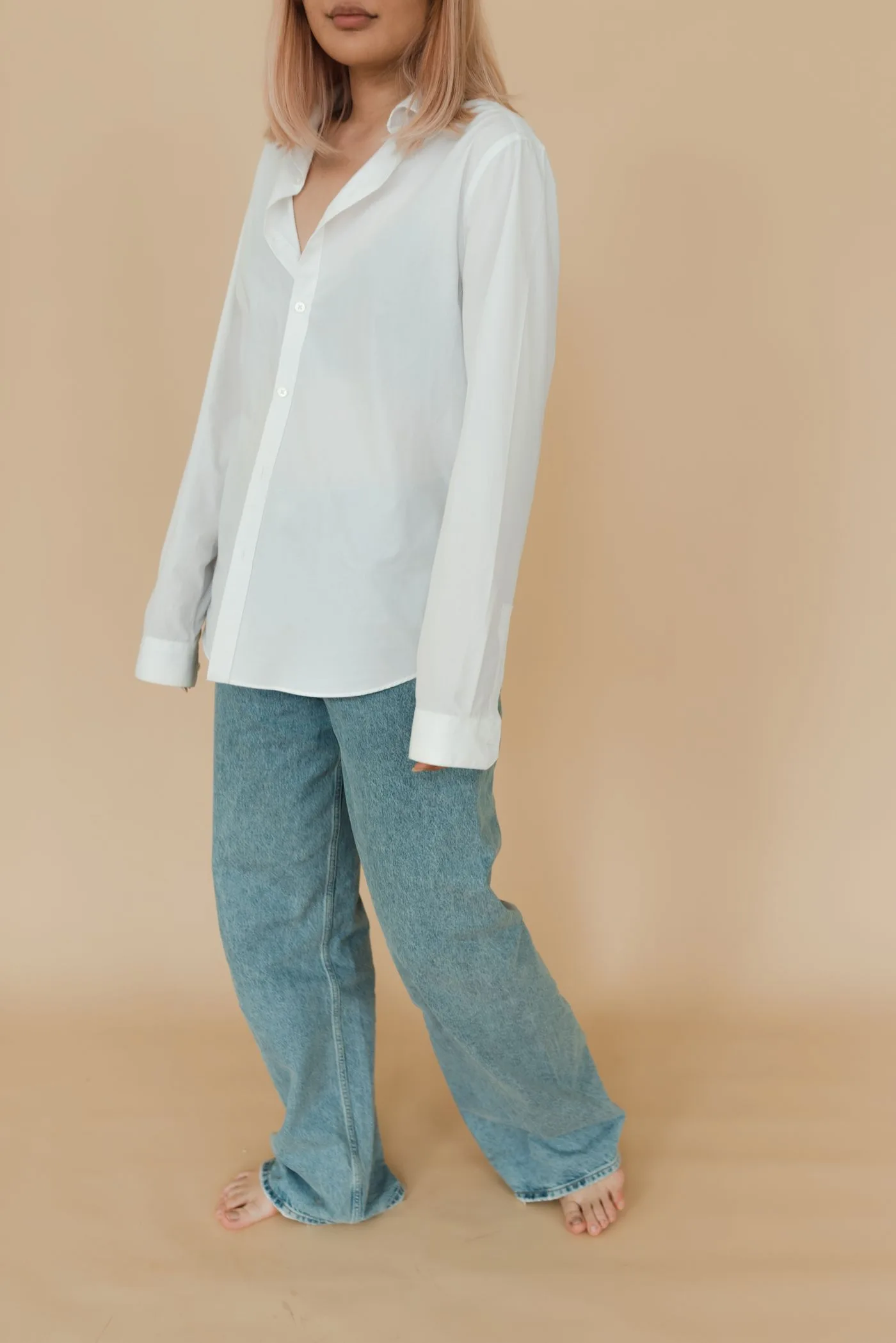 A white shirt and blue jeans worn against a warm neutral backdrop.